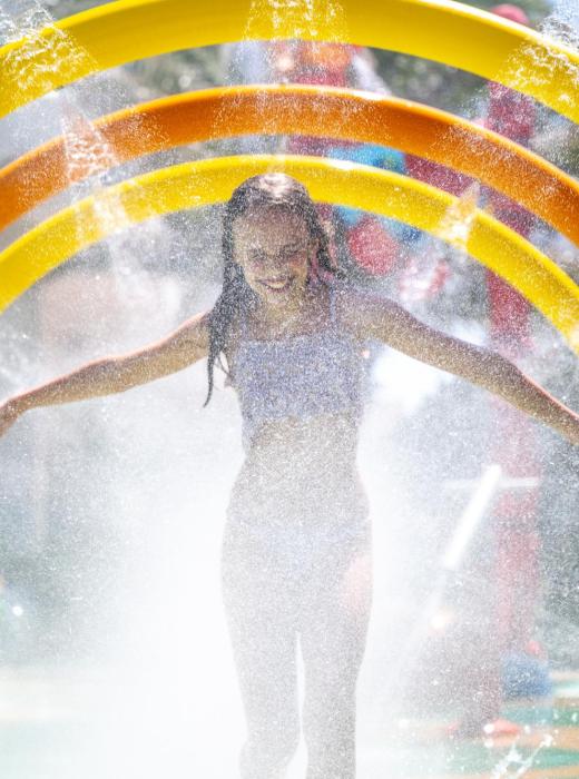 Joyful girl runs through colorful water rings in a splash park.