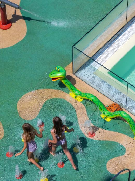 Children joyfully play with colorful water sprays in a splash park.