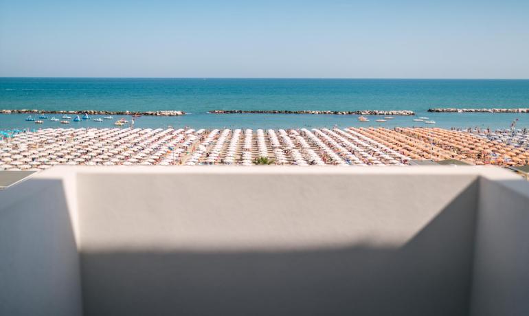 Spiaggia affollata con ombrelloni bianchi e arancioni, vista dal balcone.