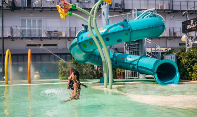 Bambina gioca in piscina con scivolo acquatico colorato.