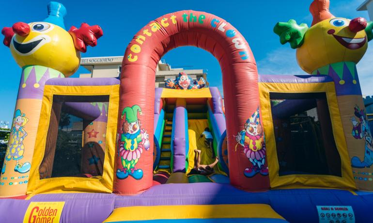 Castello gonfiabile colorato con clown e scivolo per bambini.