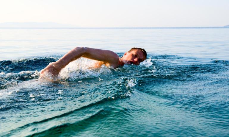 Un uomo nuota nel mare calmo, trasmettendo libertà e serenità.