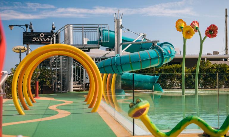 Parco acquatico con scivolo, archi gialli e decorazioni floreali colorate.