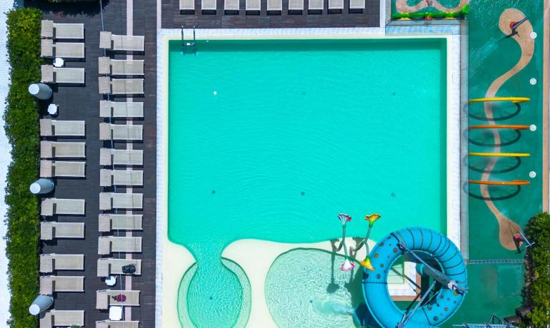 Piscina turchese con scivolo, lettini e giochi d'acqua, atmosfera di relax e divertimento.