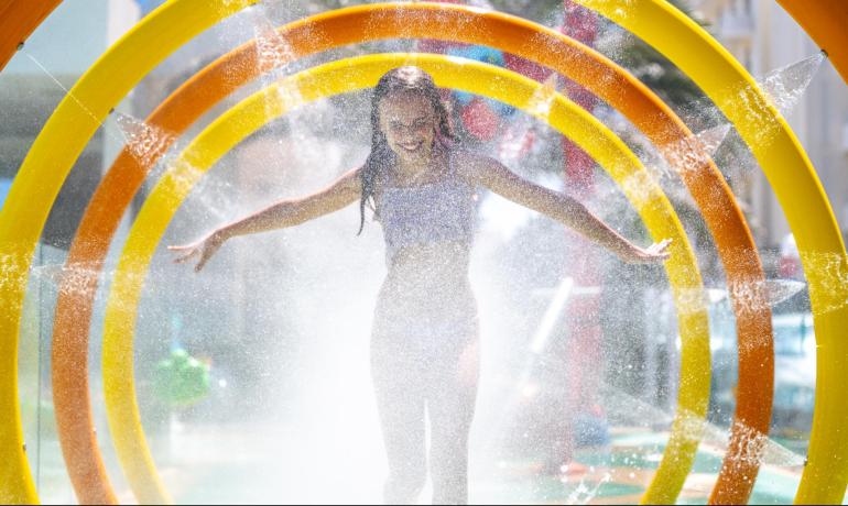 Bambina gioiosa attraversa cerchi d'acqua colorati in un parco acquatico.