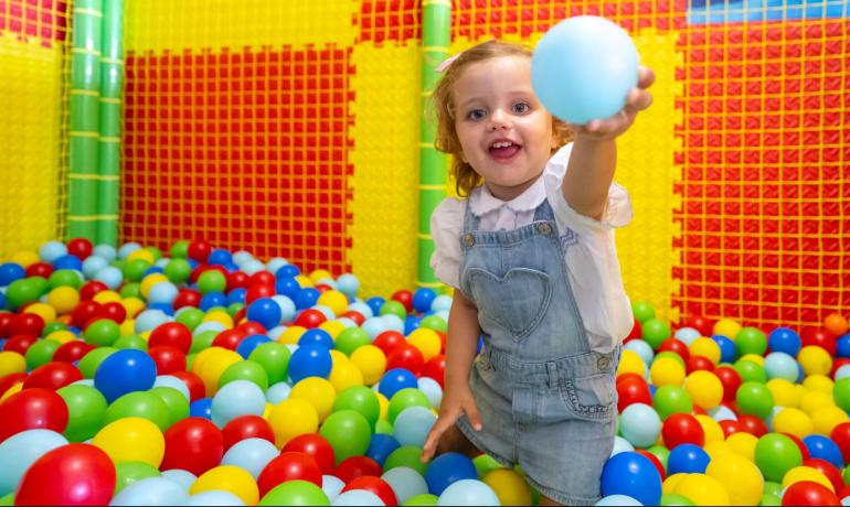 Bambina felice gioca tra palline colorate in un'area giochi vivace.