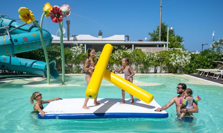 Famiglia felice gioca in piscina con gonfiabili colorati sotto il sole.
