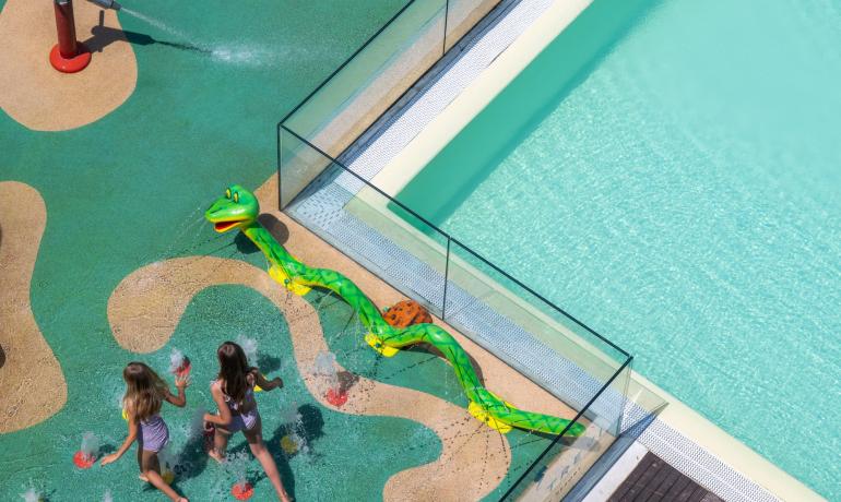 Bambini giocano felici con spruzzi d'acqua colorati in un parco giochi acquatico.