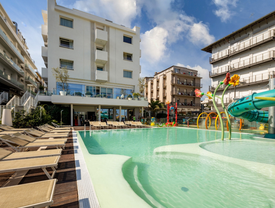 Piscina all'aperto con scivoli e lettini, circondata da edifici moderni.
