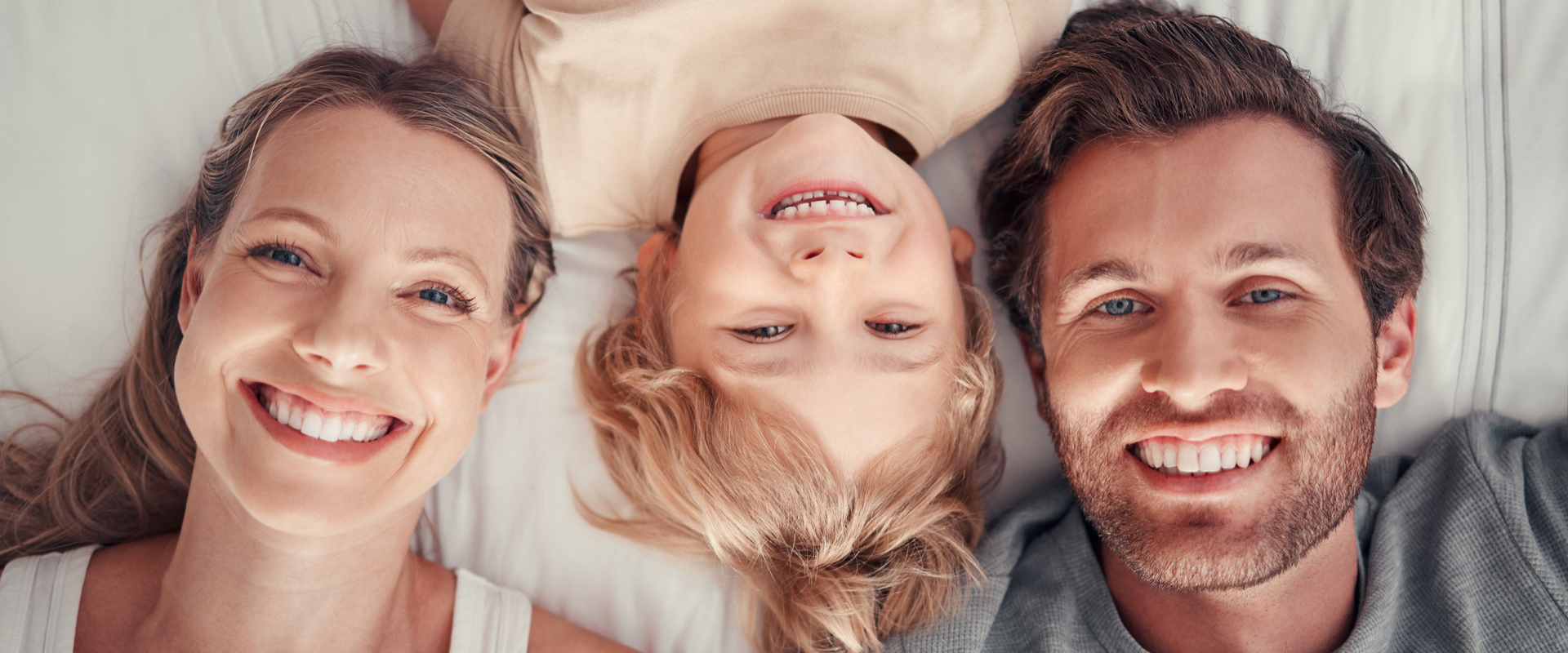 Famiglia sorridente distesa sul letto, vista dall'alto.