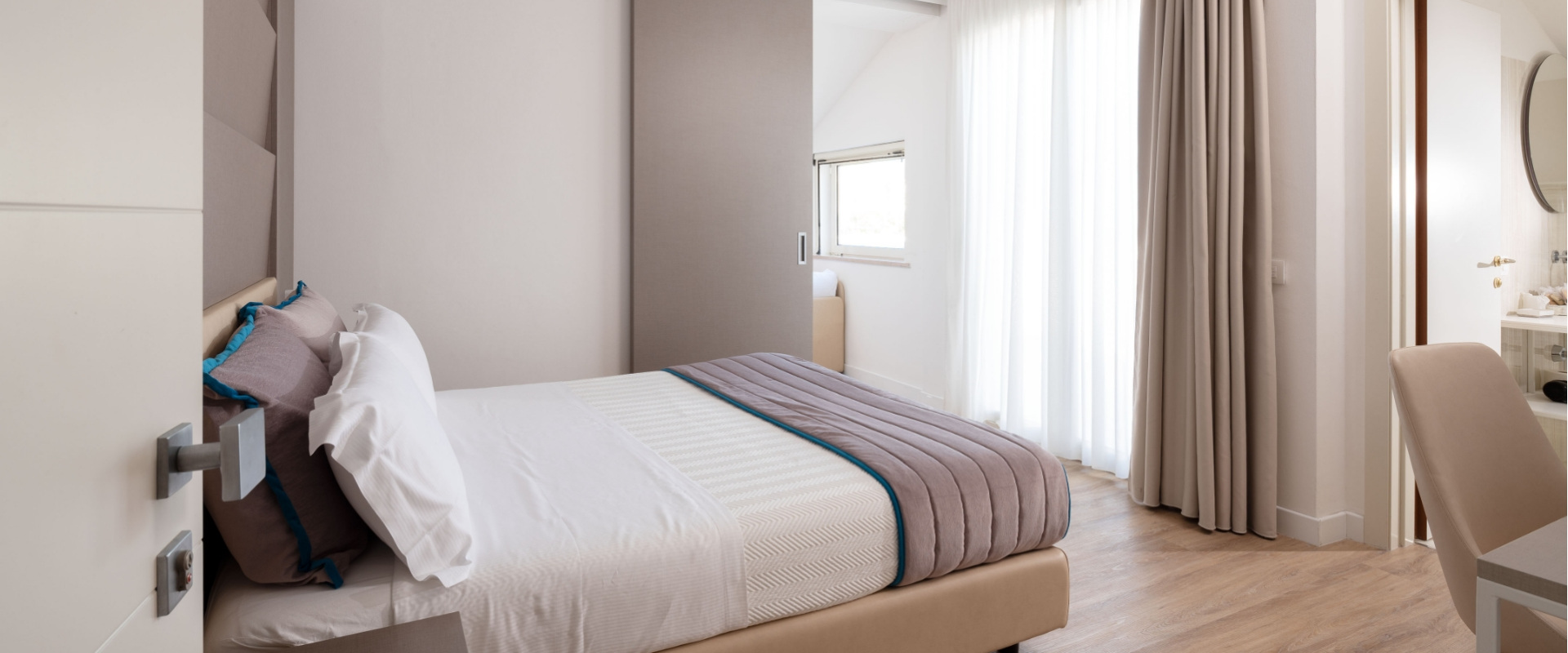 Camera moderna con letto matrimoniale, tende chiare e pavimento in legno.