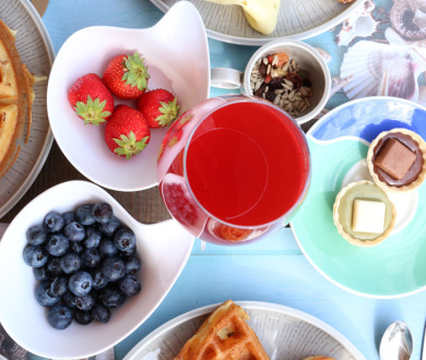 Colazione con frutta, formaggi, affettati, cornetto, dolci, succo rosso e cereali.
