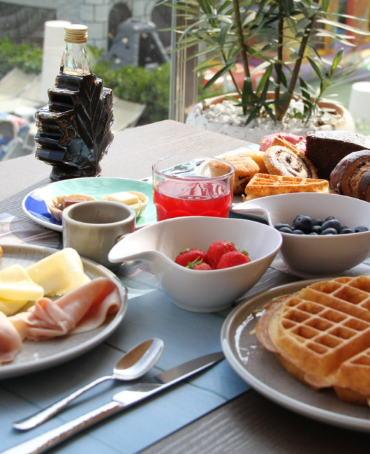 Colazione ricca con waffle, frutta, formaggi, affettati, dolci e bevande calde.