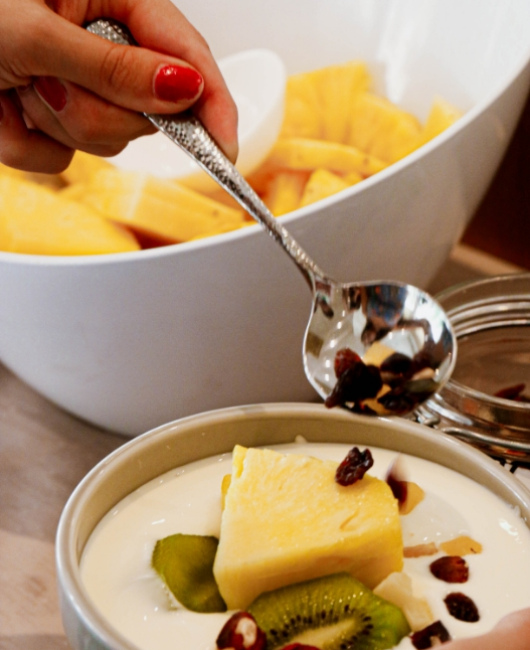 Yogurt con kiwi, ananas e uvetta, servito in una ciotola bianca.