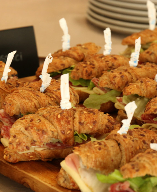 Croissant integrali farciti con prosciutto, formaggio e lattuga su un tagliere di legno.