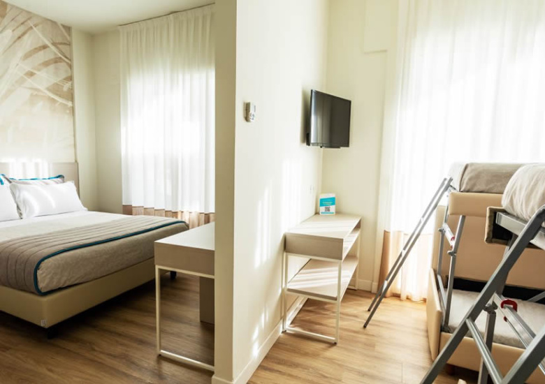 Camera moderna con letto matrimoniale e letti a castello, arredi chiari e TV.